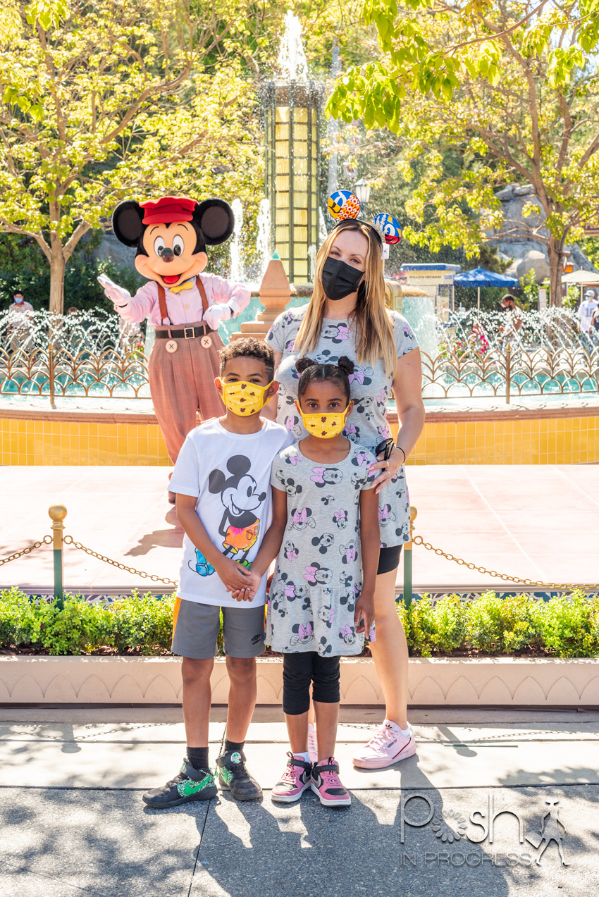 disneyland reopening |  Disneyland Reopening by popular LA lifestyle blog, Posh in Progress: image of a mom and her two kids standing with Mickey Mouse and wearing Mickey and Minnie Mouse shirts. 